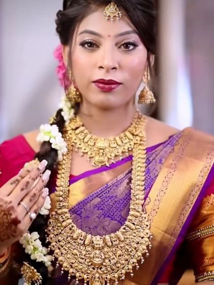 A close-up of a model wearing a layered South Indian temple jewellery set. The long haram features intricate carvings, typical of this style.