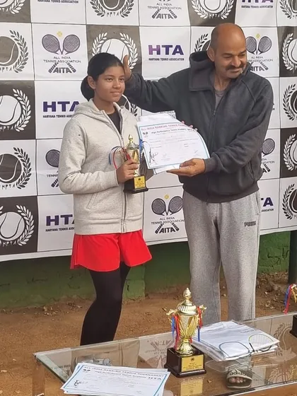 Mehr Muralidass receives her trophy for reaching her first AITA CS U-12 singles final in Gurgaon. The table is filled with trophies, highlighting the scale of the tournament.