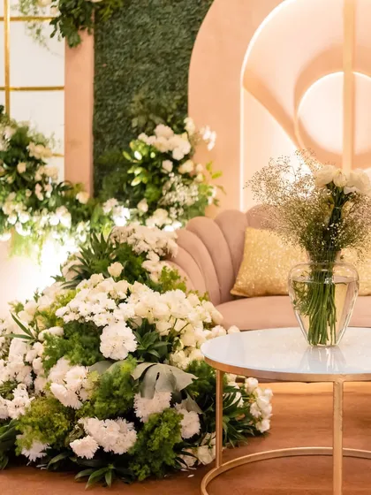 A close-up of a blush-toned, soft-glam decor setup, featuring a scalloped sofa, gold accents, and an abundance of white flowers.