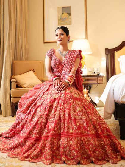 A full-length portrait of the bride in her magnificent red Rahul Mishra lehenga. The makeup is classic and elegant, perfect for a grand wedding at the Taj Mahal Palace.