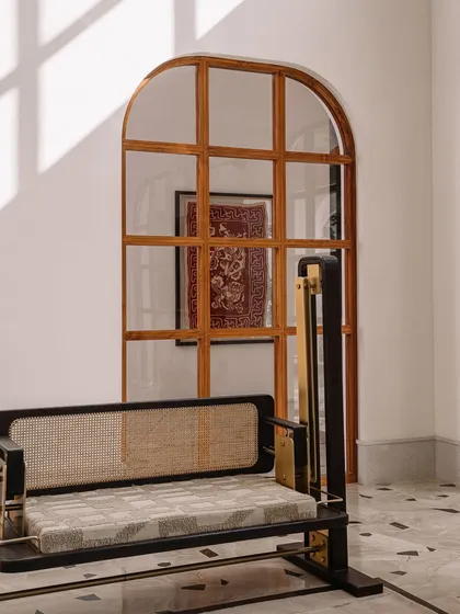 A detail shot of a sleek, modern swing with a woven cane back, set against an arched window. This piece combines traditional materials like cane and wood with a minimalist frame, showcasing our approach to contemporary Indian design.