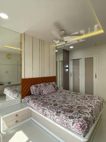 A bright and airy bedroom featuring a mirrored wardrobe that visually expands the space. The combination of a patterned headboard and subtle ceiling lights creates a sophisticated look.