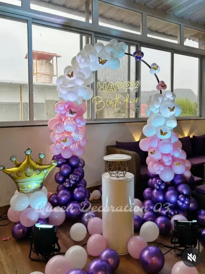 A royal-themed party with a large foil crown, a balloon arch in purple, pink, and white, and butterfly accents.