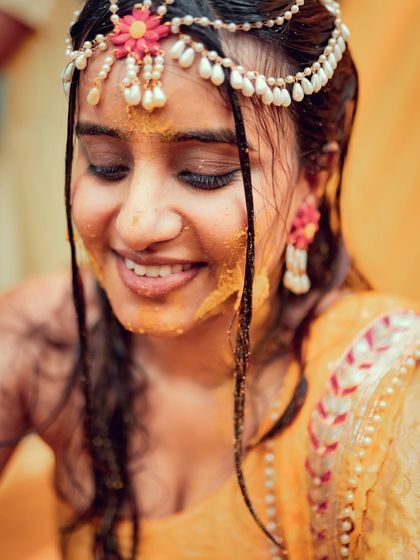 A beautiful close-up of the bride during her Haldi ceremony, capturing her serene smile and the delicate floral jewelry.