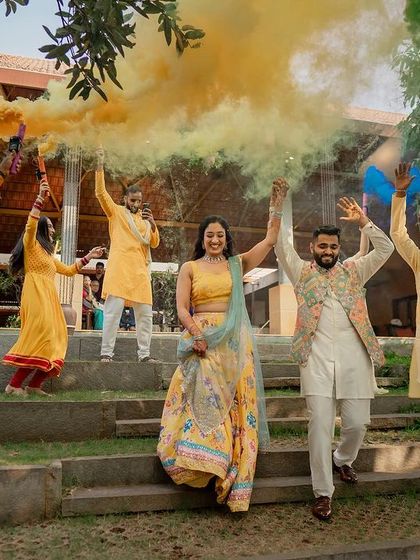 The couple makes a grand entrance to their Haldi ceremony, accompanied by friends and vibrant yellow and green smoke.