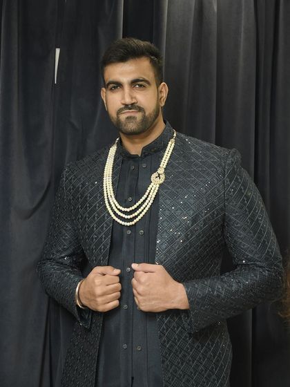 A confident pose from the client, showcasing the complete royal look with the pearl necklace against the dark Indo-western jacket.
