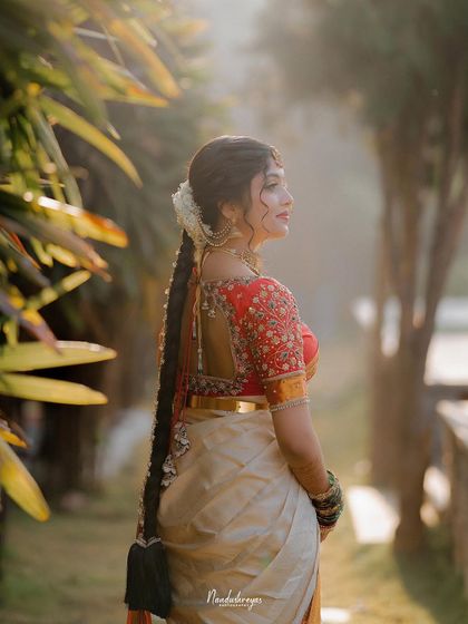 A beautiful back-profile shot of the bride, highlighting her elaborate traditional braid and the stunning design of her saree blouse.