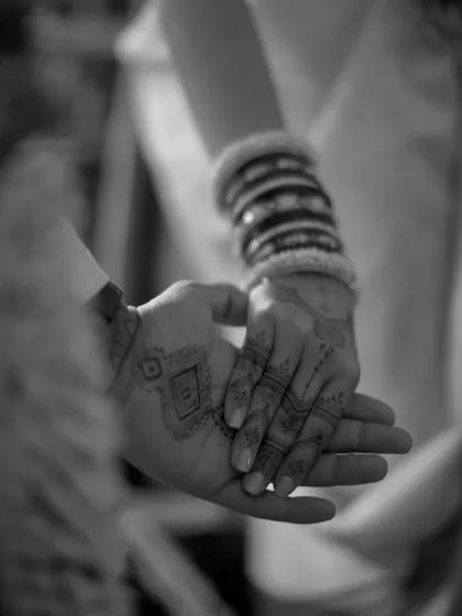 A black and white detail shot of the couple's hands, showcasing the bride's bangles and the groom's henna. A simple, yet powerful image of their union.