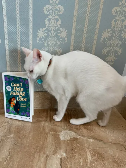 My cat giving my second novel, *Can't Help Faking in Love*, a curious sniff. She's my number one supporter (when she's not sleeping).