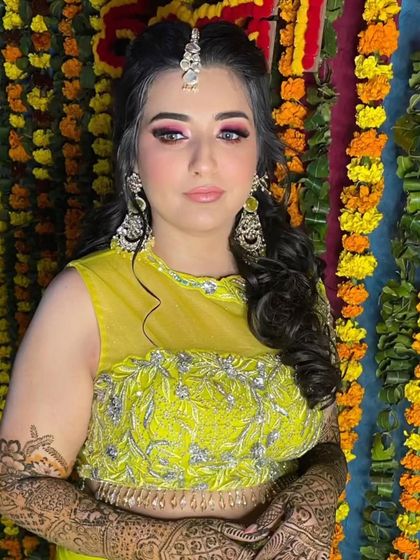 A fun and curly braided ponytail for a Mehendi look. The bright pink eye makeup and colorful background make this a super festive vibe.