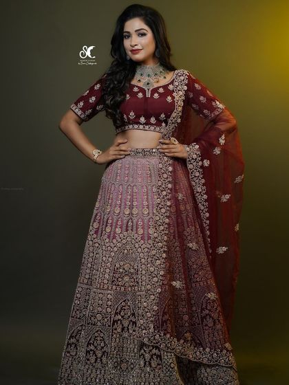 A full-length view of a royal reception lehenga. The deep maroon color and intricate embroidery are complemented by glamorous makeup and soft curls, creating a truly regal look.