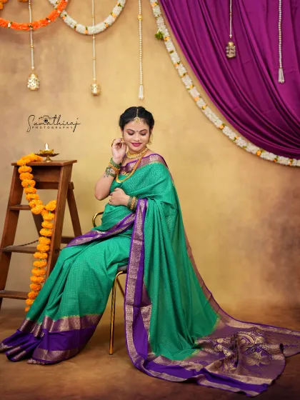A full-length portrait of a mother-to-be in a gorgeous green and purple saree. The elegant pose and traditional props like the ladder and marigolds create a festive and beautiful scene.