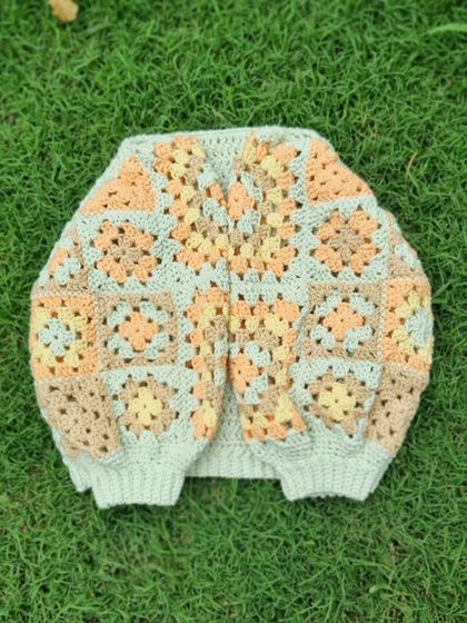 A flat-lay of the granny tee, showing the construction. The body is a simple, textured stitch, while the sleeves are made from classic granny squares in a soft, peachy color palette.