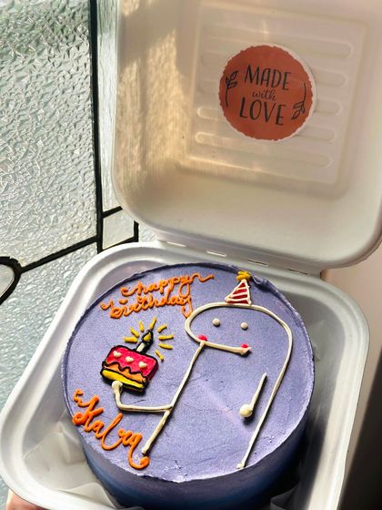 A fun bento cake with a stick figure holding a tiny cake and candle. The purple color and playful design make it a unique birthday treat.