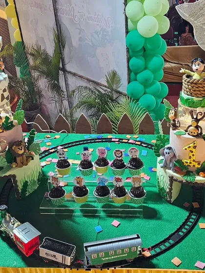 An extravagant jungle safari setup for a first birthday, featuring two large cakes, cupcakes, and a working model train.