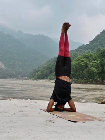 Sirsasana (Headstand) on the banks of the Ganges. This full inversion calms the brain, strengthens the core, and improves circulation, but it requires significant practice and strength to perform safely.