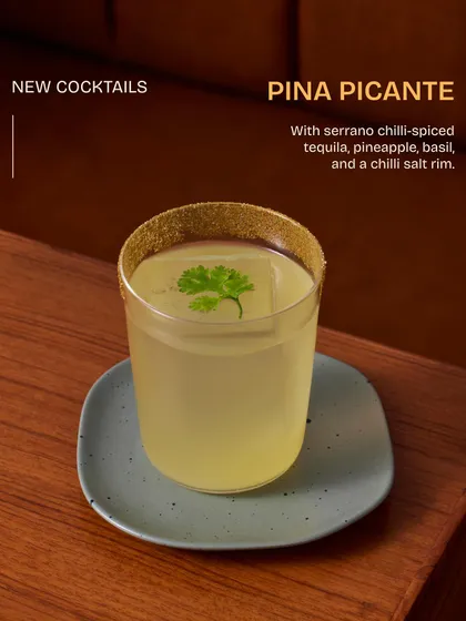 The Pina Picante, a perfect balance of sweet and heat. This drink is made with serrano chili-spiced tequila, fresh pineapple, and basil, served with a chili salt rim.