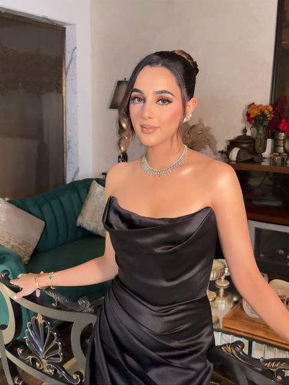 A full view of this sophisticated cocktail look. The sculpted makeup and elegant updo pair perfectly with the classic black gown for a timeless appeal.