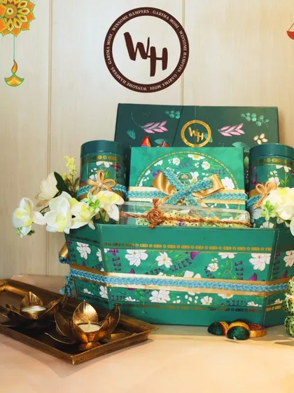 A grand festive hamper presented in a unique green floral boat-shaped basket. This arrangement is overflowing with premium teas, sweets, and decorative items, accented with white orchids and lotus-shaped diyas for a complete Diwali feel.