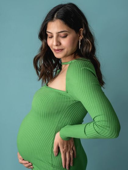 A profile shot of a pregnant mother in a striking green dress, highlighting the beautiful shape of her baby bump.
