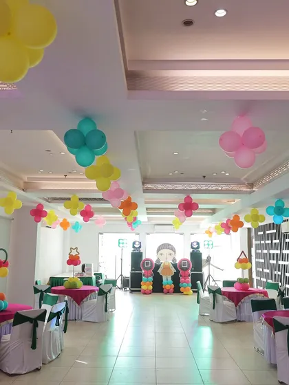 A full view of the party hall decorated for the 'Squid Fiesta'. The decor includes colorful balloon clusters hanging from the ceiling and neatly arranged table seating for the young guests.