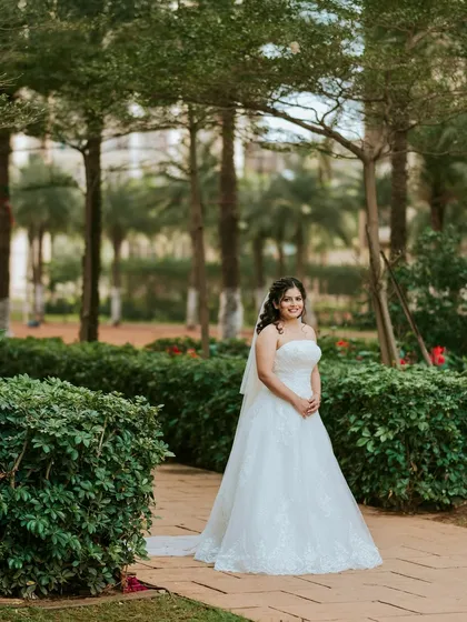 A full-length shot in a beautiful garden setting. The classic white gown and long veil are paired with a makeup look that is fresh, natural, and timeless.