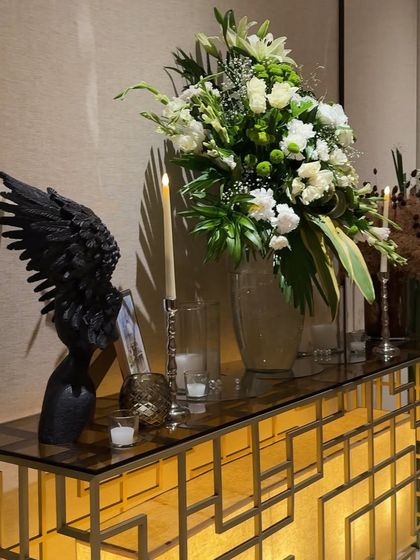 A modern and artistic console table arrangement. A large floral bouquet is paired with a unique black wing sculpture and a geometric gold console table, creating a chic and stylish vignette.