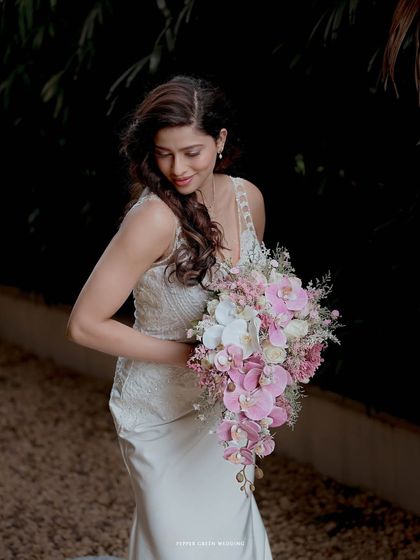 The bride looking down at her beautiful cascading bouquet of pink and white orchids, a moment of serene appreciation.