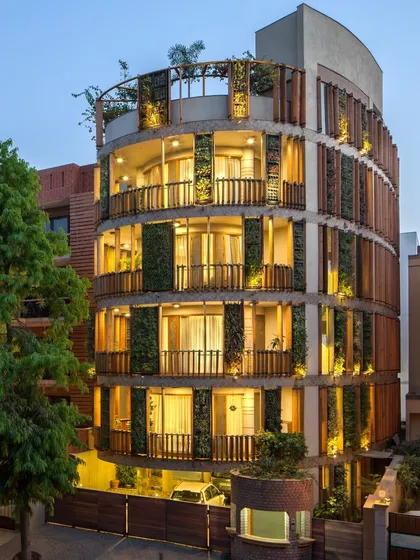 The Outré House in New Delhi, where handcrafted details and natural elements intertwine. The curved facade features a unique combination of precisely turned wooden louvres and vertical green walls, creating a living, breathing skin for the building.