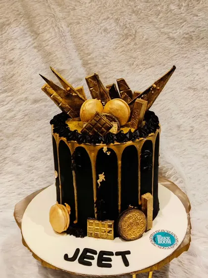A sophisticated black and gold drip cake. This design is perfect for an elegant celebration, featuring a rich black cocoa base, a shimmering gold drip, and topped with golden macarons and chocolate shards.