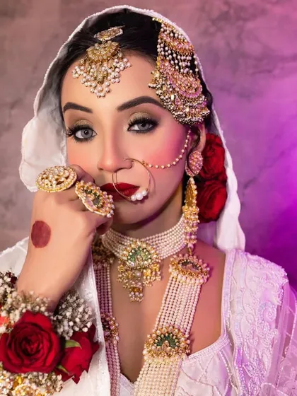 A regal Nikkah bride in a white and gold ensemble. Her look features striking blue eyes, a bold red lip, and an elaborate passa, creating a truly memorable bridal portrait.