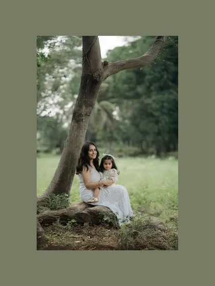 A mother and her daughter sit together under the shade of a tree in a lush green field. This portrait captures a peaceful, quiet moment of togetherness in nature, reflecting a calm and steady bond.