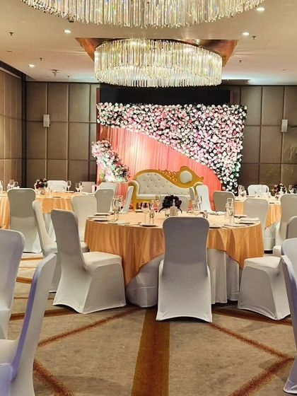 This engagement or reception stage features a full wall of pink and white flowers. The simple yet stunning floral backdrop provides a beautiful setting for photos inside a banquet hall.