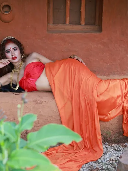A reclining pose that showcases the full length of the draped saree. The framing with natural foliage adds to the organic and earthy feel of the 'Lahu Munh Lag Gaya' series.