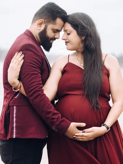 An intimate close-up of the couple embracing on the beach, their hands gently holding the baby bump, capturing a moment of shared love.