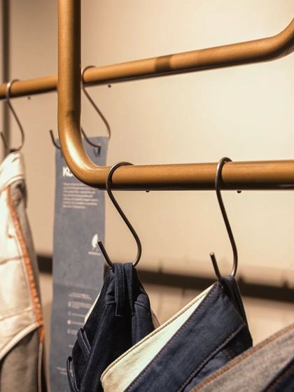 A detail of the custom clothing rail at Bombay Shirt Company, where the antique brass finish and S-hooks add a touch of bespoke elegance.