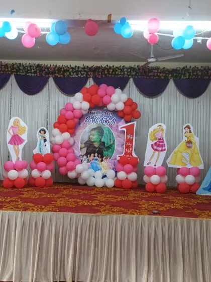A grand 3D Princess theme stage decoration for a first birthday party. The setup includes multiple princess cutouts like Barbie, Jasmine, and Elsa, a balloon arch, and a personalized photo backdrop.