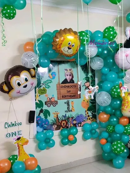 A personalized jungle-themed first birthday. The backdrop includes a photo of the birthday boy, 'Chinkoo', surrounded by a green balloon frame and various animal character cutouts.