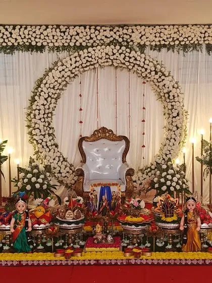 A baby shower setup with a grand floral ring as the backdrop. The plate decoration is symmetrical and elegant, flanked by traditional lamps.
