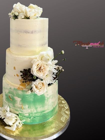 Another angle of the sage and white wedding cake. This view shows the delicate arrangement of fresh flowers and the subtle shimmer of gold leaf against the buttercream.