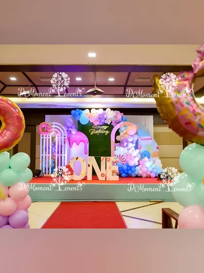 A wide shot of the Candyland-themed stage, flanked by large donut foil balloons on pastel balloon pillars. The red carpet leads the eye to the vibrant and sweet-filled backdrop.