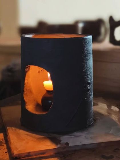 A student-made ceramic candle holder glows warmly in the studio. In our classes, you will learn to create functional pieces like this, focusing on form, cut-outs for light, and finishing techniques.