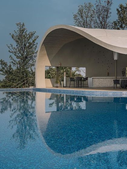 The fluid lines of the pool's edge and the curved roof create a dynamic interplay of shapes. This view shows how the structure provides shelter while remaining open, offering a modern interpretation of a natural cave.