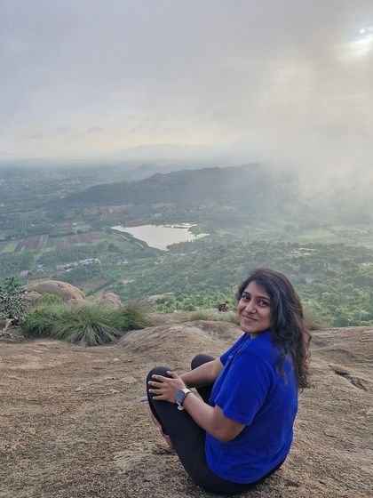 A trekker sits on the edge, enjoying the vast view from Uttari Betta.
