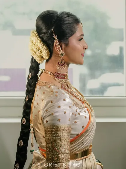 A side profile of a bride showcasing her elaborate bridal hairstyle and the detailed embroidery on her off-white silk blouse. The craftsmanship of the blouse complements her traditional look.