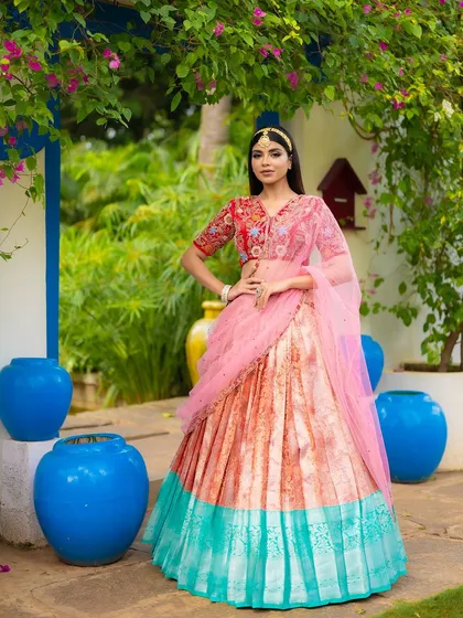 A full-length shot of a designer half saree against a beautiful garden backdrop. The composition showcases the entire outfit, from the embellished blouse to the flowing skirt.