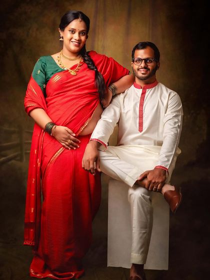 A full-length portrait of a couple during their traditional maternity session. The vibrant red saree and classic posing create a powerful and timeless image.