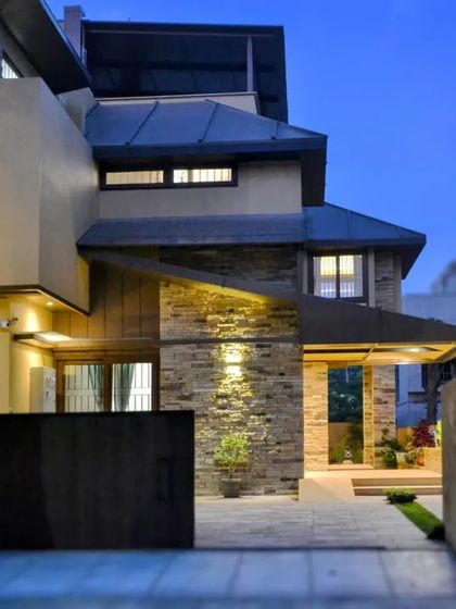 As night falls, the architectural lighting transforms the house, accentuating the texture of the stone cladding and the geometric lines of the overhangs.
