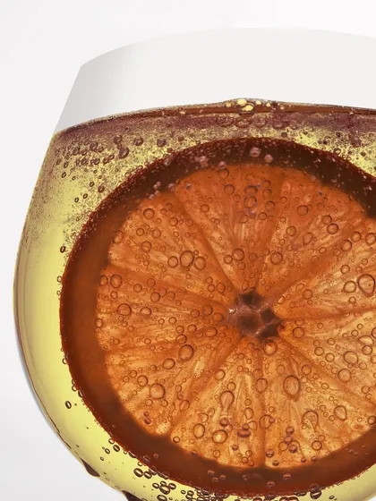 A wider view of the summer cocktail. You can see the shape of the glass and the way the light passes through the bubbly liquid, backlighting the orange slice.