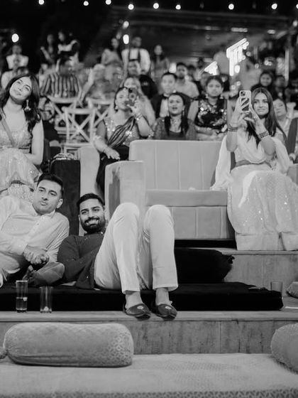 Friends relaxing and watching the Sangeet performances. This candid shot captures the casual, real moments that happen throughout the wedding.